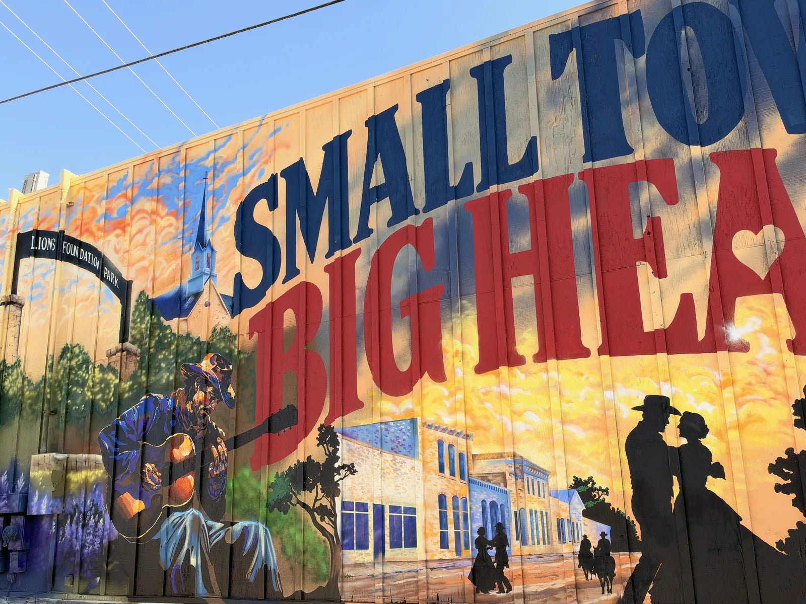 The finished SMALL TOWN BIG HEART mural on the Parkers wall, seen at an angle with silhouettes strolling downtown