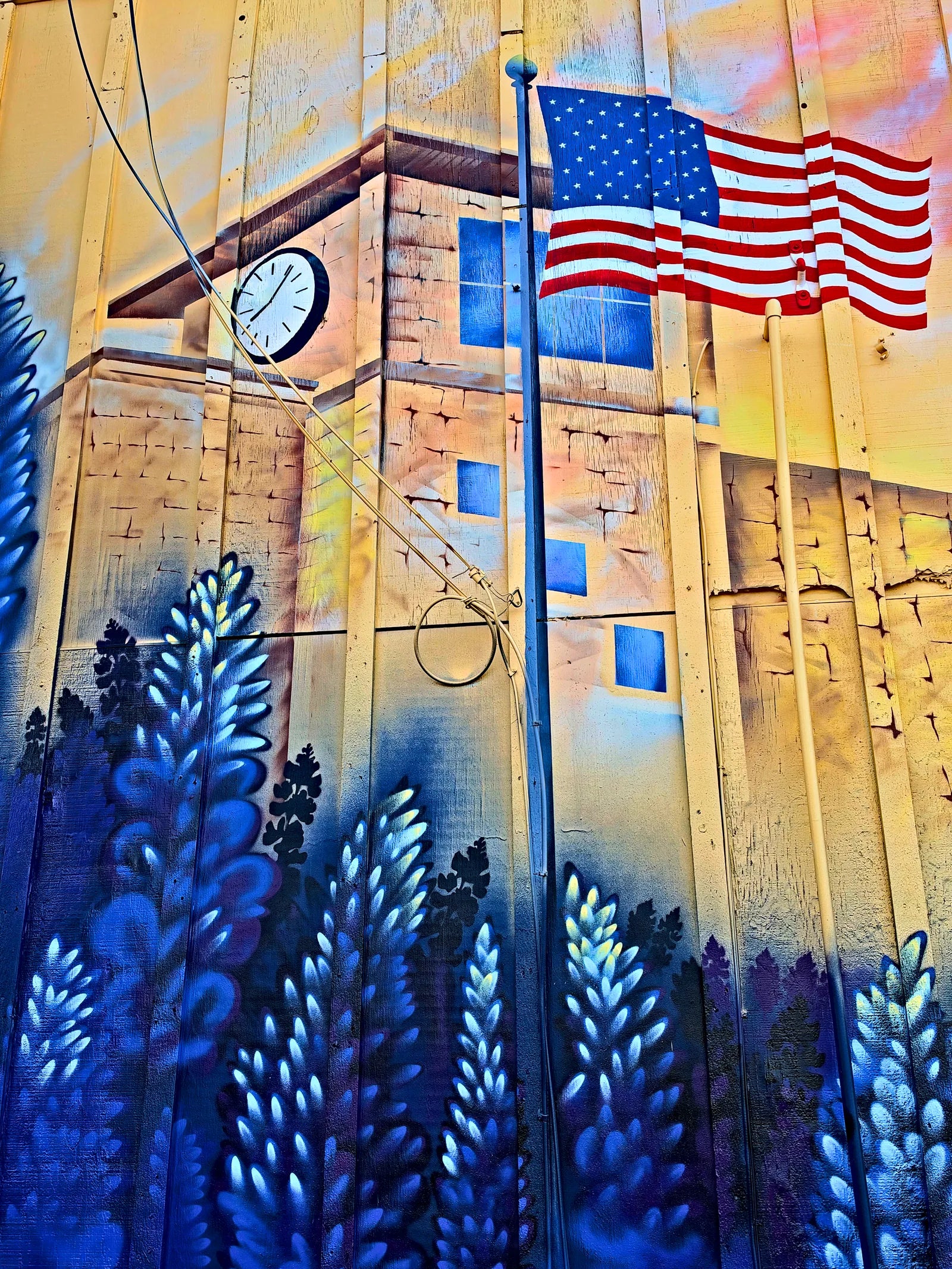 Clock tower and US flag above a field of bluebonnets on the Parkers mural