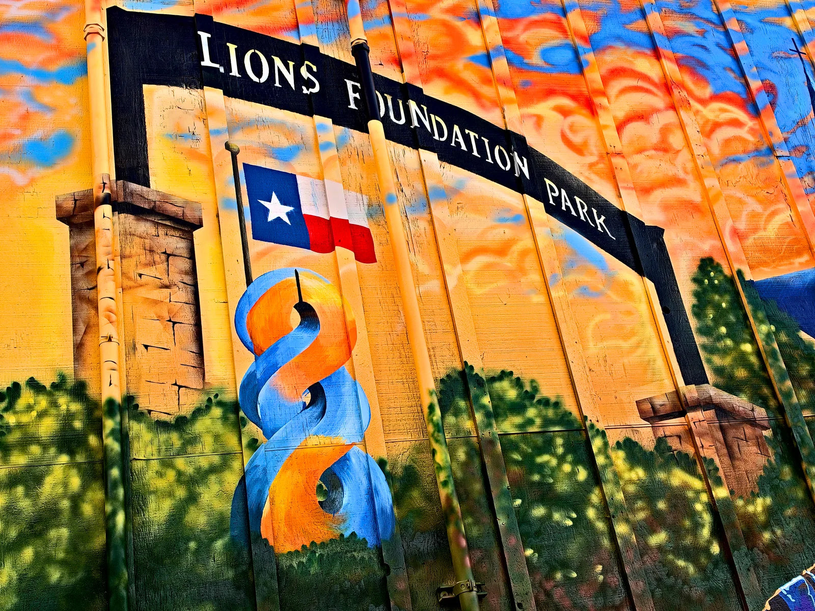 Lions Foundation Park arch with the Texas flag and the orange and blue 8 ribbon